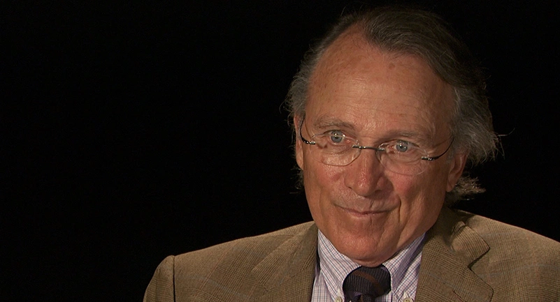 Glen Urban seated in front of a black background for an on camera interview, smiling.