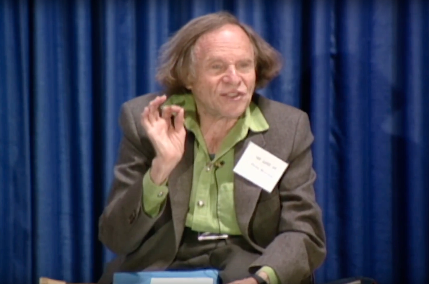 Philip Morrison giving speech on stage, blue curtain in the background